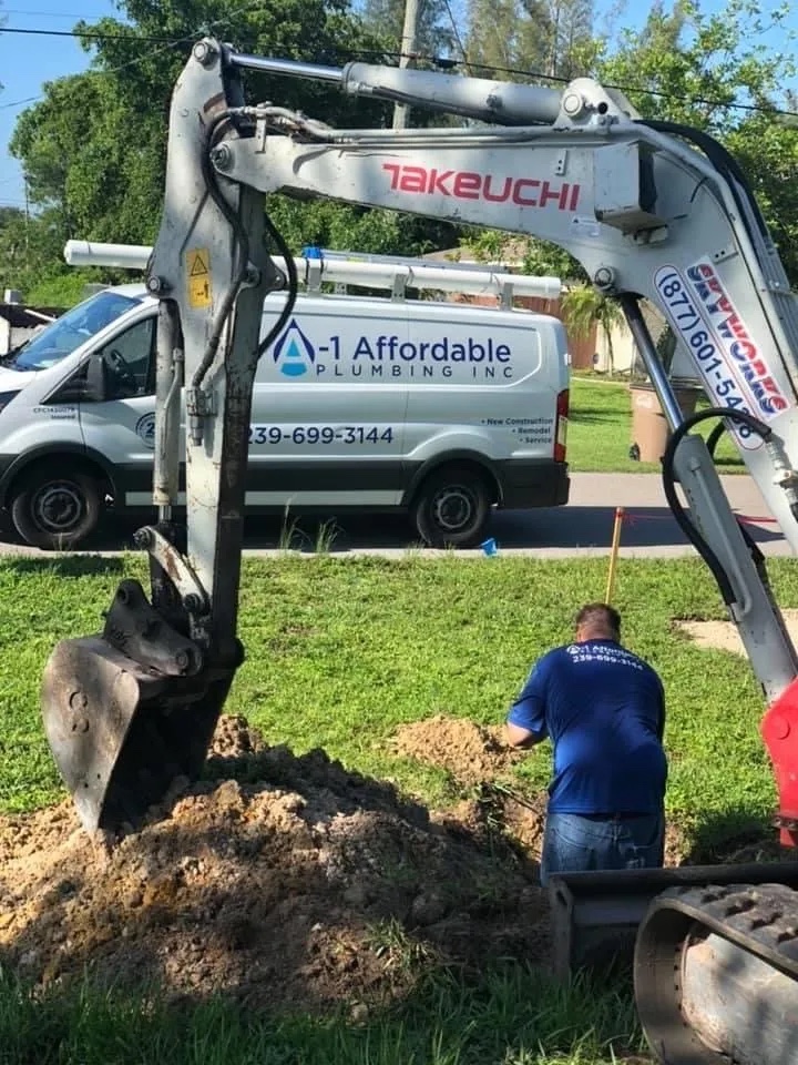 Plumber standing in a hole dug by an excavator to locate a sewer line at a residential property